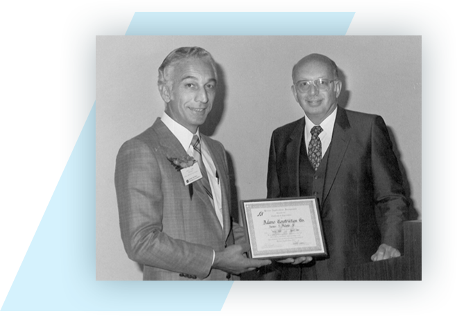 Black and white photo of Adamo's founder posing with a certificate next to another man
