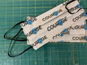 Photo of cloth face masks that say "Courage" on them with the Adamo logo as the A in courage