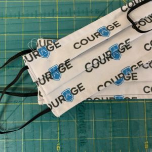 Photo of cloth face masks that say "Courage" on them with the Adamo logo as the A in courage