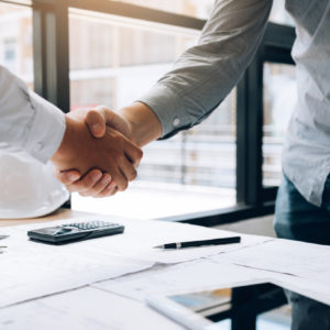 Two people shaking hands over a desk covered in construction plans