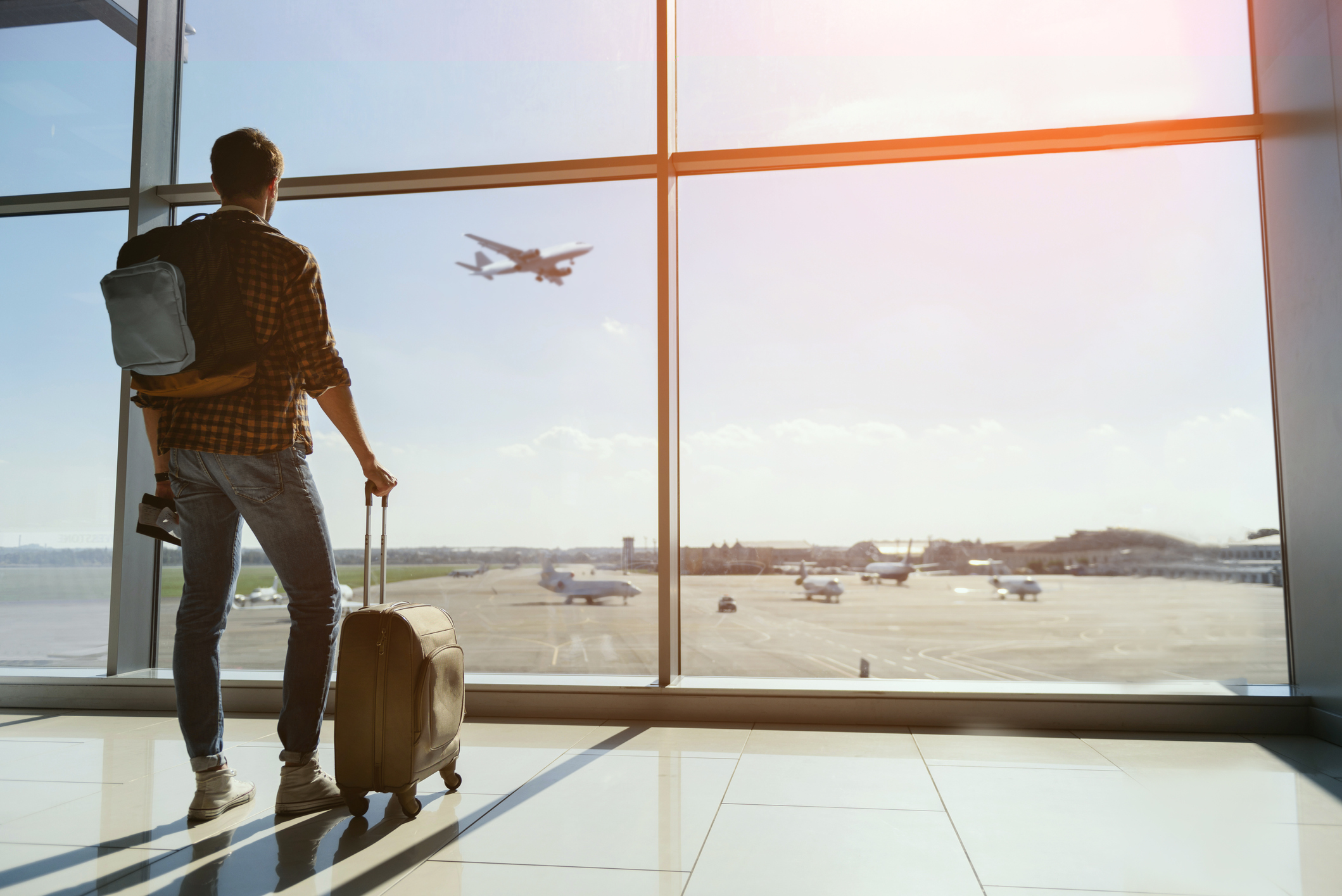 Man at airport with suitcase watching a plane through the window