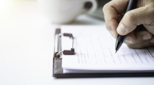 A close up of a hand holding a pen hovering over a form on a clipboard