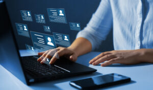 Closeup of hands scrolling on a laptop with a graphic of personnel badge icons in front of the computer