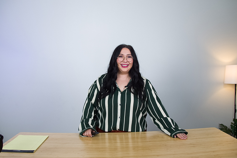 A woman standing behind a desk in front of a white backdrop