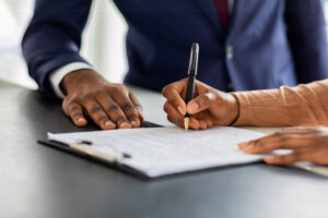 A close up of two people's hands as one of them signs a document with a pen