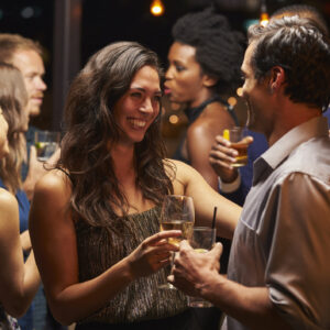 A man and a woman chat and laugh at a busy party with drinks in hand