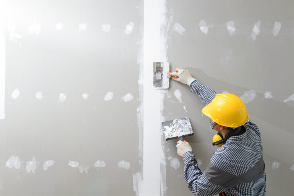 A person in a yellow construction hat adding plaster to an unfinished wall