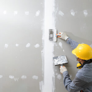 A person in a yellow construction hat adding plaster to an unfinished wall