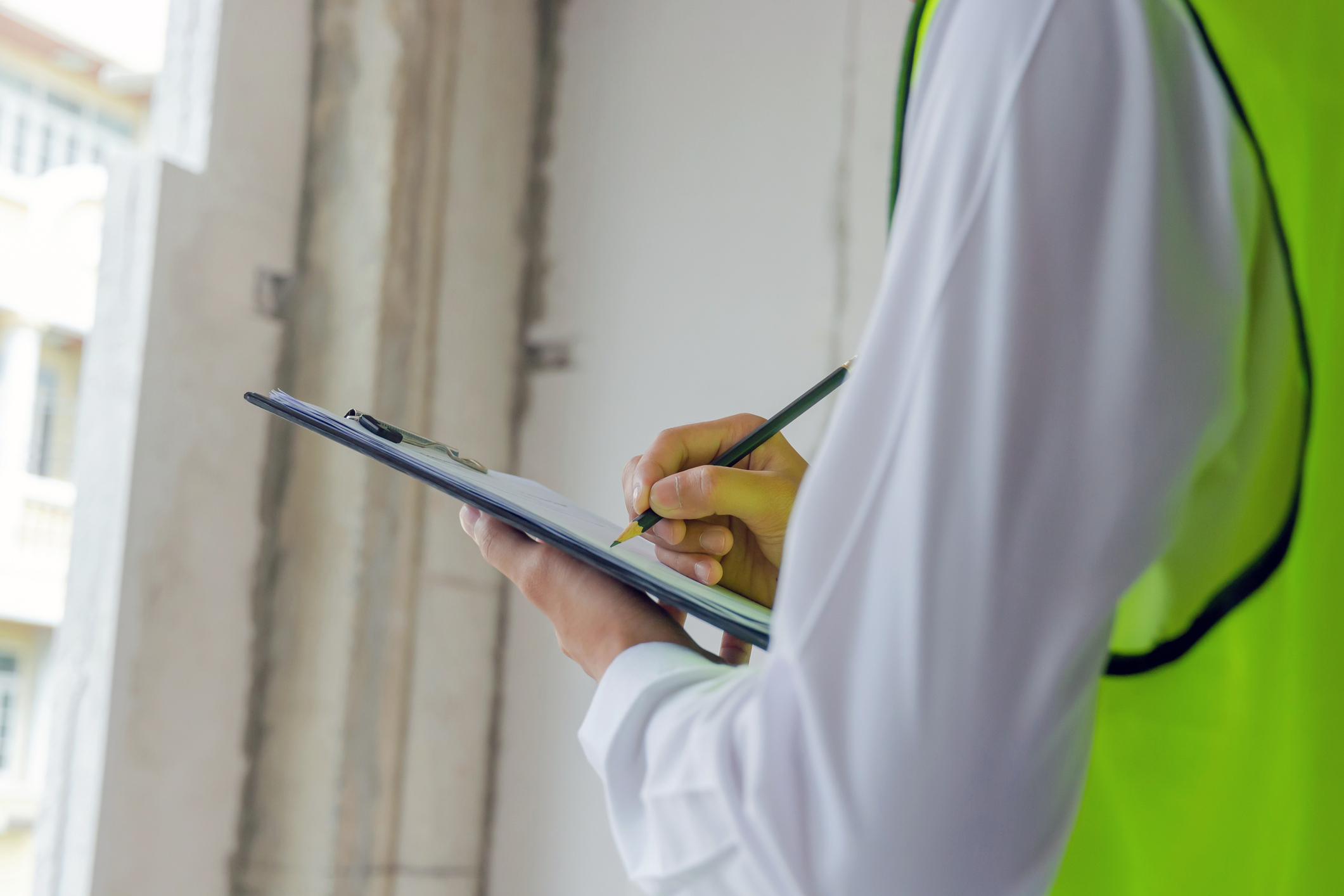 Shoulders down photo of a person in a green safety vest holding a clipboard, checking things off