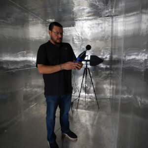 A man with a microphone performs acoustic testing in a room covered in RF foil