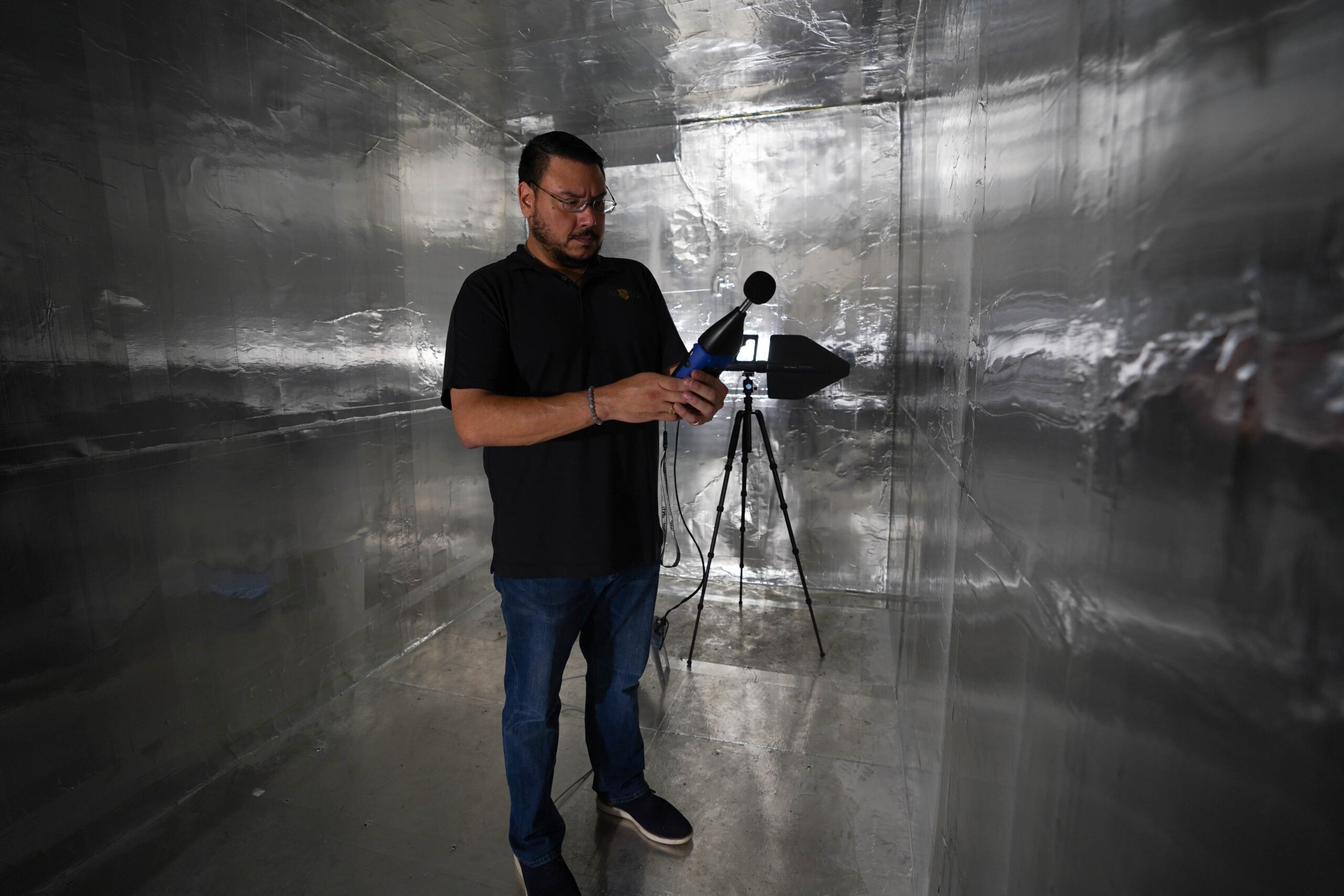A man with a microphone performs acoustic testing in a room covered in RF foil