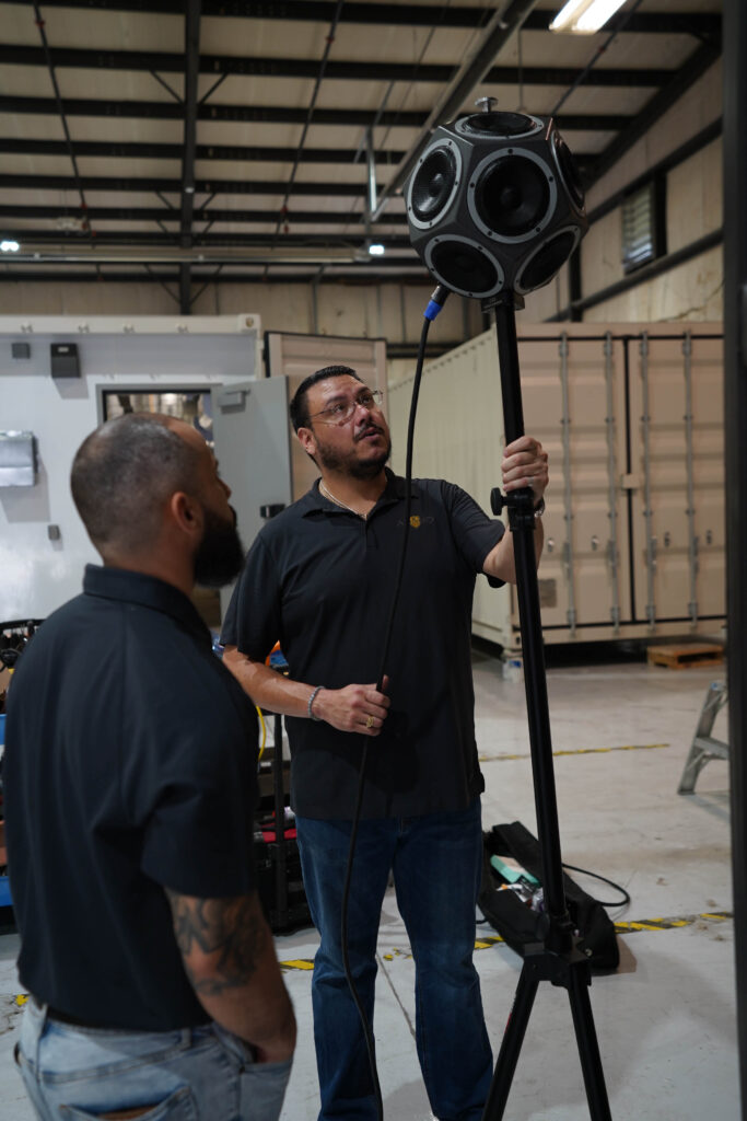 Two men in a warehouse looking at a 12-sided speaker used in acoustic testing