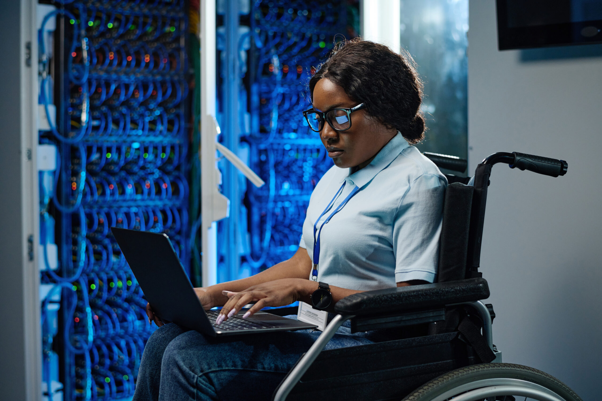 A woman in a wheelchair in a server room with a laptop on her lap